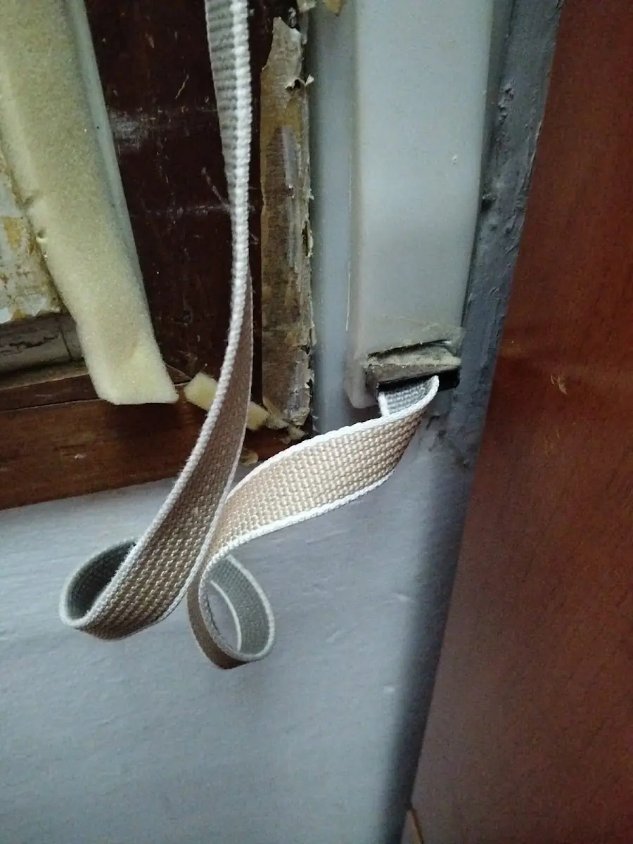 Cinta de persiana desgastada en una ventana con marco de madera